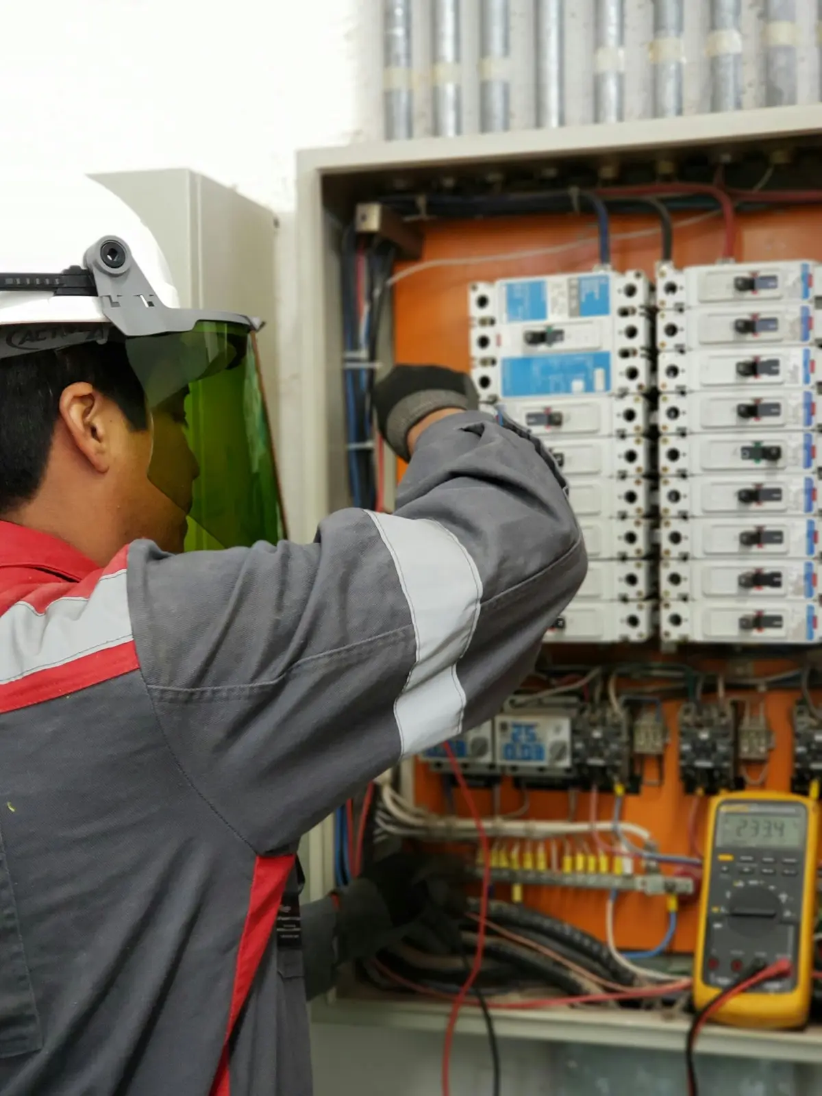 Electricista con casco y careta revisando un tablero eléctrico